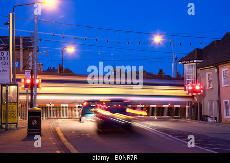 Temps d'EXPOSITION DE COLCHESTER EAST RAIL GATES CROSSING DE NUIT AVEC UN TRAIN QUI PASSAIT ET LES BARRIÈRES VERS LE BAS. Banque D'Images