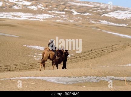 La neige dans le désert Taklimakan province du Xinjiang en Chine de l'ouest avec deux hommes Ouïghours croisement avec chameau de Bactriane Banque D'Images