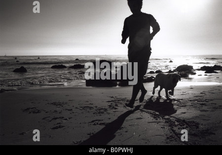 Silhouette of man running on beach with dog on shore horizontale noir et blanc sable Banque D'Images