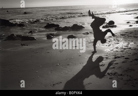 Silhouette of man doing cartwheel a une seule main sur la plage de sable sur la rive horizontale noir et blanc Banque D'Images