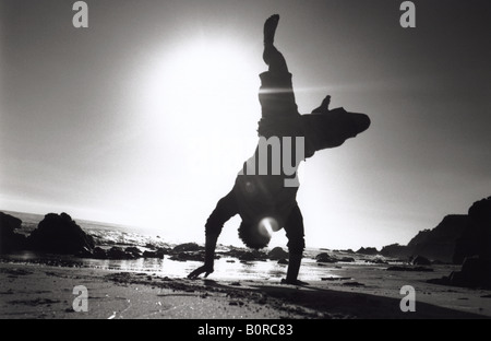 Silhouette of man doing cartwheel sur plage de sable sur la rive horizontale noir et blanc Banque D'Images