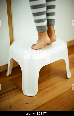 Quatre ans, fille des pieds sur le tabouret pour atteindre l'évier salle de bains Banque D'Images