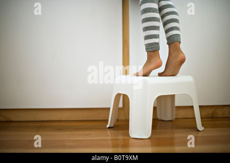 Quatre ans, fille des pieds sur le tabouret pour atteindre l'évier salle de bains Banque D'Images