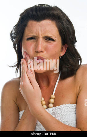 Une jeune femme souffrant de maux de dents ou de la bouche douloureuse maladie type d'ulcère se frotter sa joue pour le soulagement de douleur, UK Banque D'Images