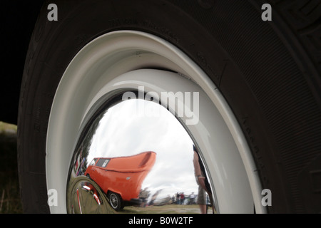 Un moyeu de roue chrome VW présente le reflet d'une autre VW Transporter orange garé à proximité. Banque D'Images