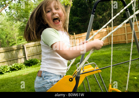 Petite fille sur balançoire, regardant la caméra heureusement qu'elle est gelée en mouvement dans les airs, avec de longs cheveux voler. Banque D'Images