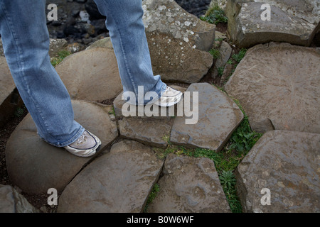 Jambes de femme portant des jeans et des vieilles baskets sur basalte rouge rock formations hexagonales à la Chaussée des géants du nord du comté d'Antrim Banque D'Images