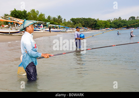 Vieux Pêcheur debout dans la mer près de Senggigi pour les petits poissons de pêche à la ligne en utilisant des méthodes traditionnelles, de l'île Lombok, Sunda moindre I Banque D'Images