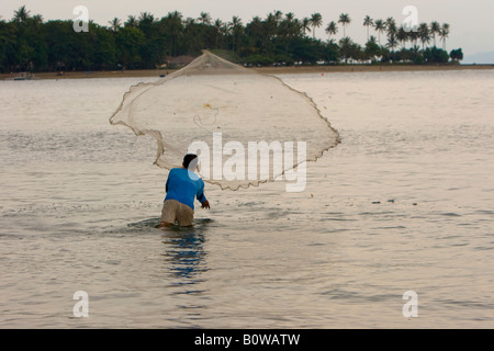 Fisherman casting son filet dans une baie à temps le soir, l'île de Lombok, Indonésie, Îles de la sonde Lesser Banque D'Images