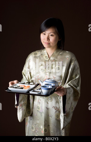 Une femme dans un kimono portant un plateau de sushi et plateau Banque D'Images