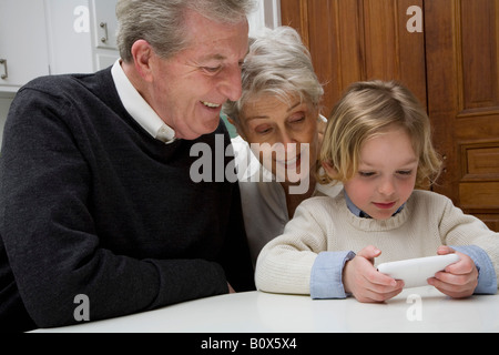 Un petit-fils à l'aide d'un appareil électronique tandis que ses grands-parents watch Banque D'Images