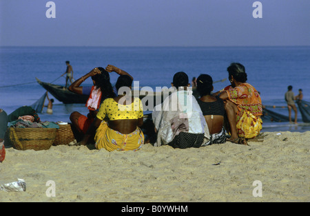 Les femmes dans des vêtements colorés s'asseoir sur le sable et regarder les hommes apportent dans les poissons PLAGE DE BENAULIM GOA INDE Banque D'Images