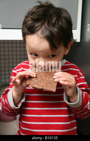 Mauvais parent d'un enfant de 3 ans d'être à haute voix pour manger une grande plaque de chocolat Banque D'Images