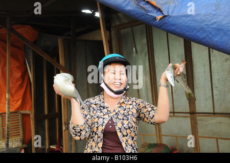 Femme vietnamienne souriante portant un casque d'écrasement tenant des poissons à vendre à Hoi An marché du poisson Vietnam Banque D'Images