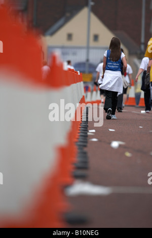 Concurrent femelle marche dernières ligne de cônes de circulation utilisé pour boucler parcours du marathon Banque D'Images