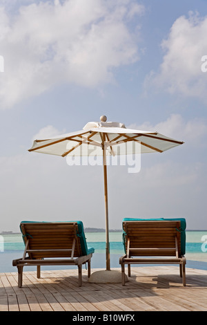 Chaises longues donnant sur la piscine à débordement et le lagon de Anantara Resort aux Maldives Banque D'Images