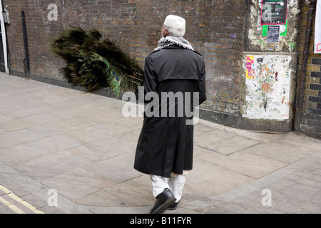 Personnes âgées l'homme du Bangladesh avec des plumes de paon dans Brick Lane London England Banque D'Images