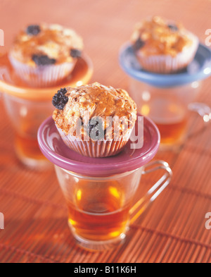 Muffins Raisin faits maison avec tasse de thé chaud en verre sur fond de tapis de table en paille naturelle. Délicieux petits gâteaux sucrés. Pâtisserie froide de jour d'hiver Banque D'Images