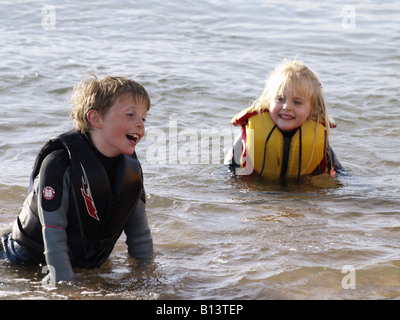 Jeune garçon et fille, porter une combinaison isothermique et aides à la flottabilité, jouer dans la mer. Banque D'Images