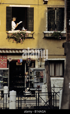 Jeune femme assise dans une fenêtre d'hôtel avec un bloc de croquis à Venise Italie Banque D'Images