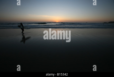 Un internaute tête pour attraper les dernières vagues de la journée à la plage de Sennen, Cornwall. Banque D'Images