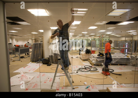 Vitrier vérifie une cloison en verre sur un site de construction en voie d'achèvement Banque D'Images