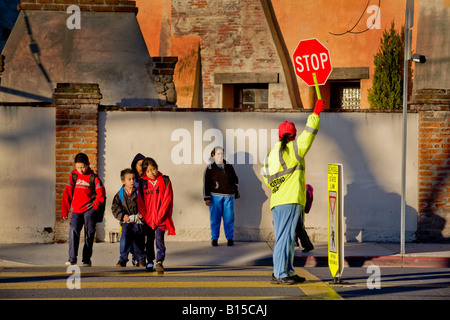 Brigadier scolaire hispanique rue des contrôles de trafic que les élèves de l'école élémentaire de la Californie du Sud et les parents arrivent en AM Banque D'Images