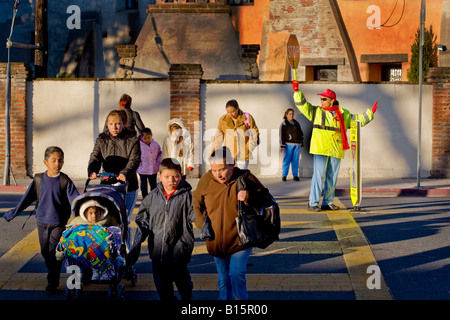 Brigadier scolaire hispanique rue des contrôles de trafic que les élèves de l'école élémentaire de la Californie du Sud et les parents arrivent en AM Banque D'Images