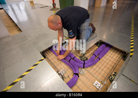 Un ingénieur réseau fixe grosses liasses des câbles de données sous le plancher dans un bâtiment nouvellement construit. Banque D'Images