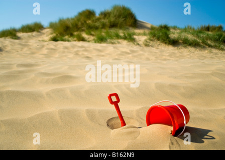 Close up of Horizontal un godet en plastique rouge et chat dans les dunes de sable sur une journée ensoleillée Banque D'Images