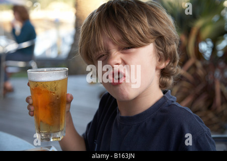 Jeune garçon enfant assis fièrement dans son restaurant holding shandy prétendant une bière Banque D'Images