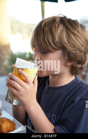 Jeune garçon enfant assis fièrement dans son restaurant holding shandy prétendant une bière Banque D'Images