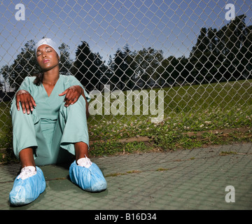 African female Nurse sitting against fence Banque D'Images