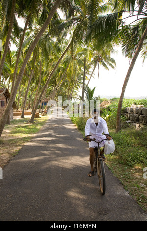 Un homme rides le long de la route étroite qui mène à Muzhappilangad dur en plage située à proximité de Thalassery au Kerala. Banque D'Images