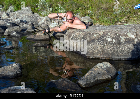Jeune homme allongé sur son ventre en prenant une photo proche du front de mer au lac Isteren, Hedmark, Norvège Banque D'Images