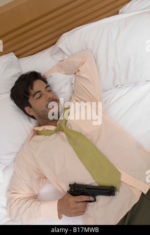 Hispanic businessman holding gun in bed Banque D'Images