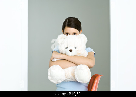 Preteen girl hugging Grand ours en peluche, peeking at camera Banque D'Images