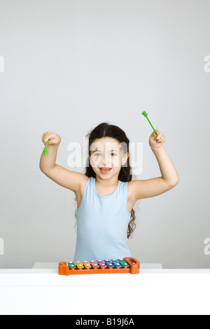 Petite fille jouant du xylophone, bras levés, looking at camera Banque D'Images