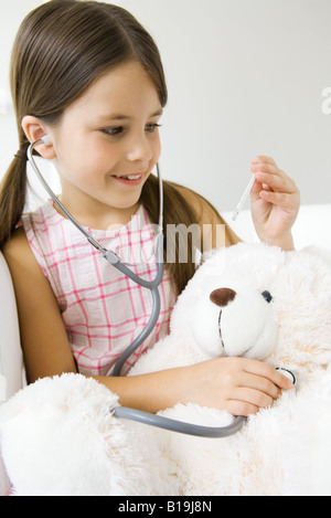 Petite fille à l'écoute du cœur de l'ours en peluche avec stéthoscope, thermomètre à Banque D'Images