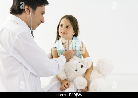 Pédiatre à l'écoute de girl's heart avec stéthoscope, girl holding teddy bear Banque D'Images