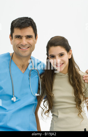 Médecin avec bras autour de l'épaule de preteen girl, les deux smiling at camera Banque D'Images