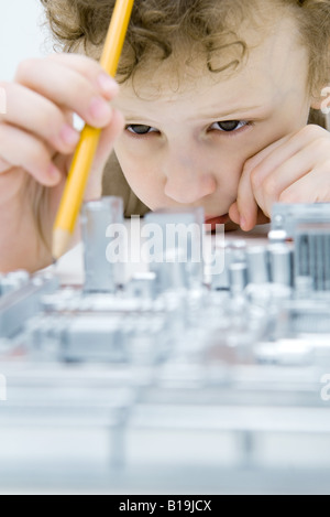 Little Boy looking at circuit board, holding pencil, close-up Banque D'Images