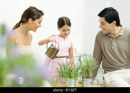 Petite fille d'arroser les plantes en pot, les parents, tous les smiling Banque D'Images