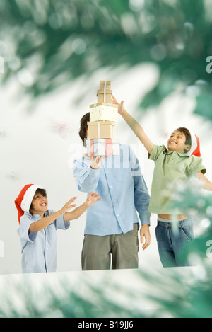 Male holding pile de cadeaux de Noël, deux garçons l'atteinte, la vue à travers les branches d'arbre de Noël Banque D'Images