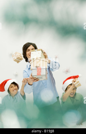 Homme transportant pile de cadeaux de Noël, les garçons d'atteindre et d'éparpiller, smiling Banque D'Images
