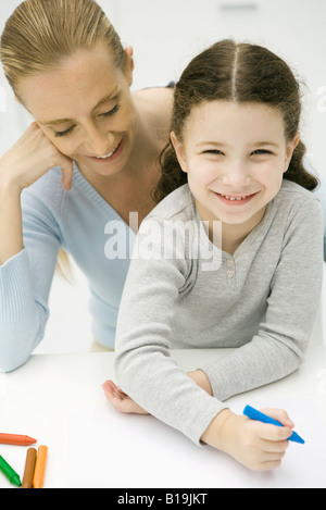 Petite fille assise sur les genoux de sa mère, colorant, smiling at camera Banque D'Images