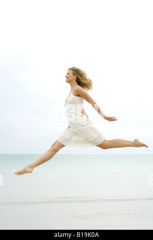 Femme sautant en l'air à la plage, vue latérale Banque D'Images