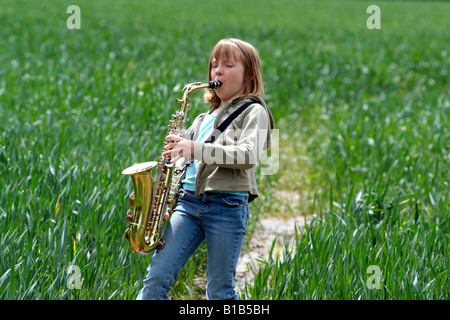 Petite fille jouant du saxophone dans un champ de cultures marche à travers la campagne anglaise Banque D'Images