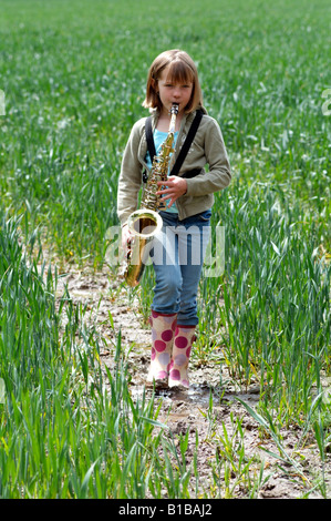 Petite fille jouant du saxophone dans un champ de cultures marche à travers la campagne anglaise Banque D'Images