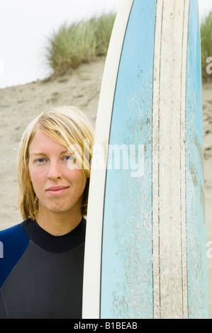 Surfeur Blond femme en combinaison avec le bleu avec un surf plage du nord-ouest du Pacifique dans l'arrière-plan. Banque D'Images